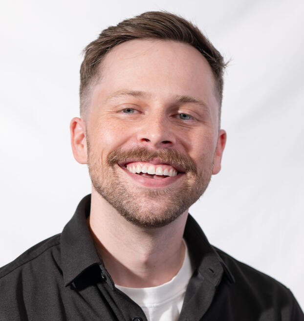 Headshot of man smiling with black dress shirt on and white background